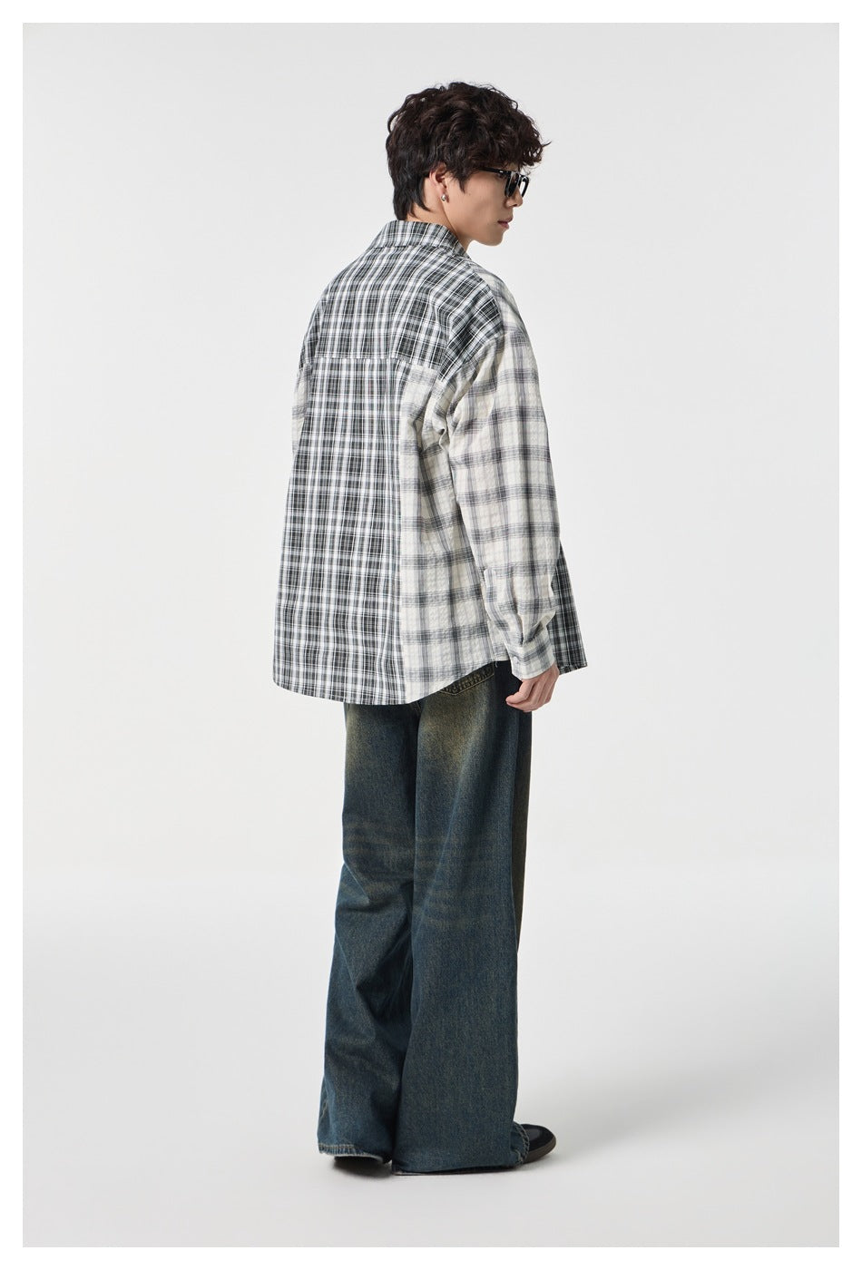 Rear view of a model wearing a loose black and cream mixed-plaid button-up shirt.