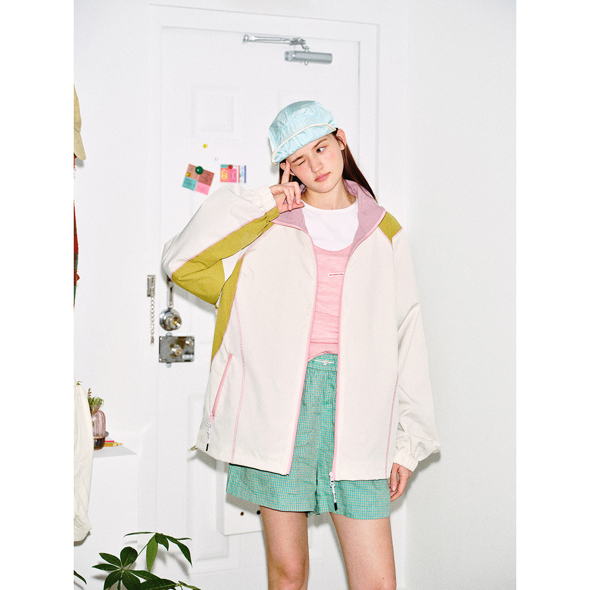 Closer view of a model wearing an ivory jacket with pink piping, olive panels and a high collar, over a pink top.