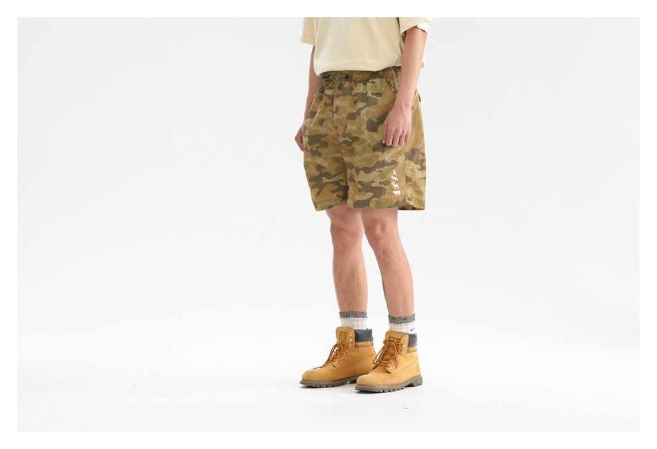 Side view of a person wearing tan camouflage shorts with white animal motif, cream tee and yellow boots