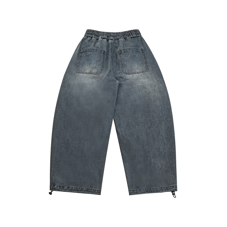Back view of faded blue wide-leg denim pants with elastic waistband, two patch pockets and hem toggles