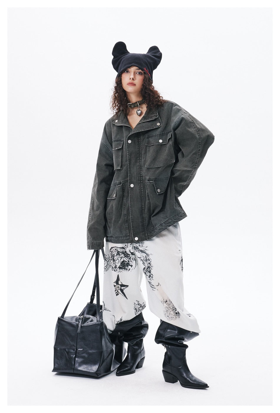 Full-length model wearing a charcoal utility jacket, white graphic trousers, black boots and a black beanie.
