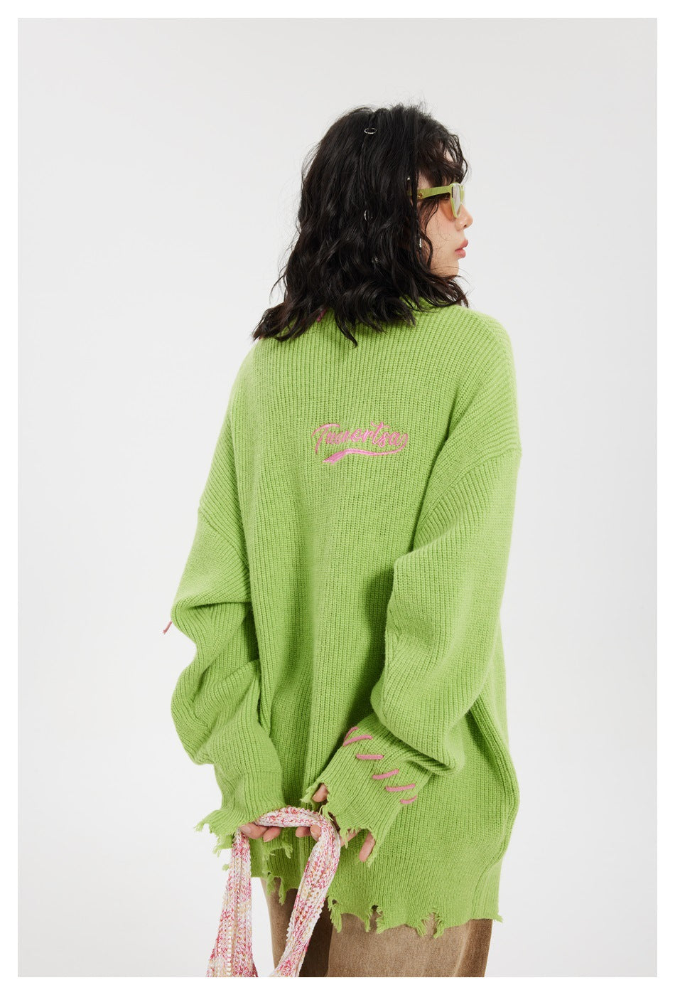 Rear view of a model wearing a lime-green distressed sweater with pink script embroidery and pink stitch accents.