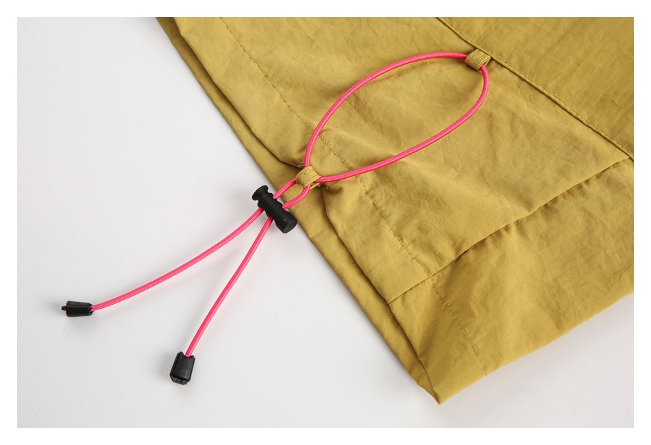 Close-up of the mustard shorts' lower edge and adjustable pink drawcord with black toggle and end caps.