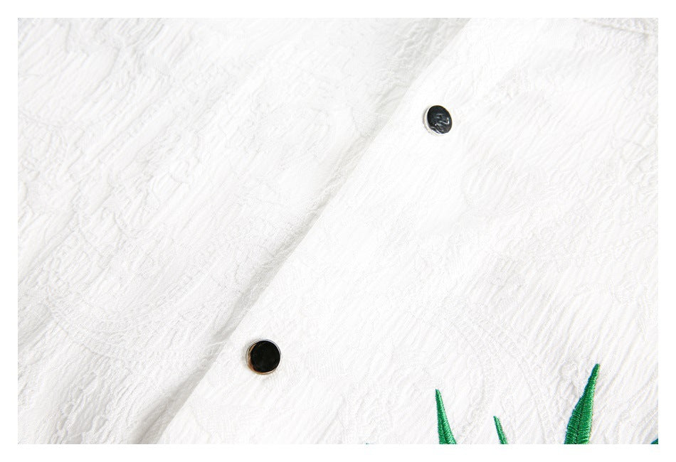Close-up of the white shirt's textured fabric, black snap buttons and a small section of green embroidery.