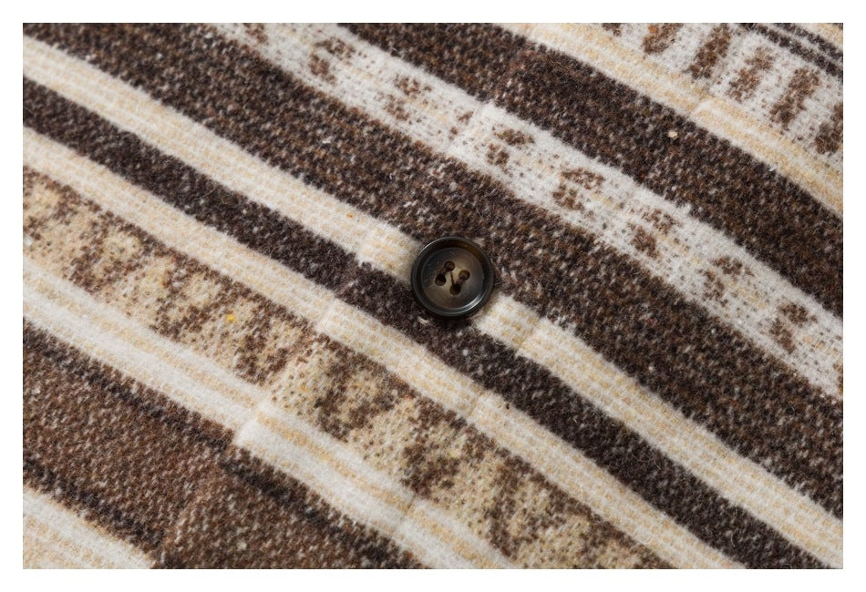 Close-up of a dark button on brown, cream, and tan striped fabric.