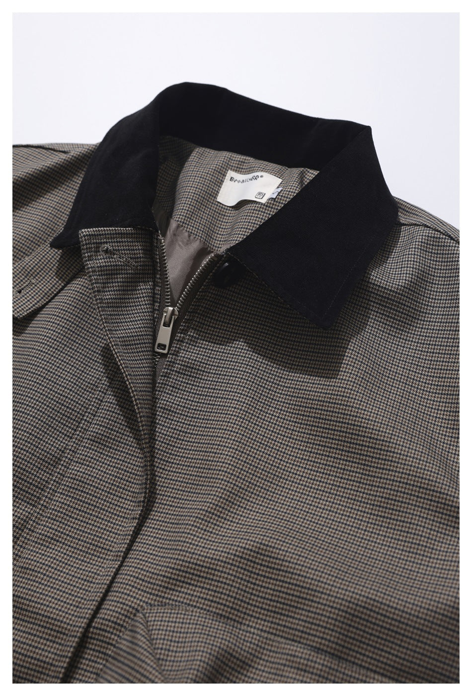 Close-up of a brown houndstooth jacket with a contrasting black collar, front zipper, and neck label.