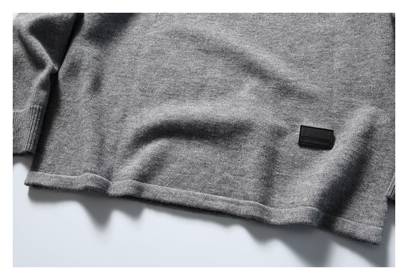 Close-up of the lower hem of a heather gray knit sweater, with a small black rectangular patch.