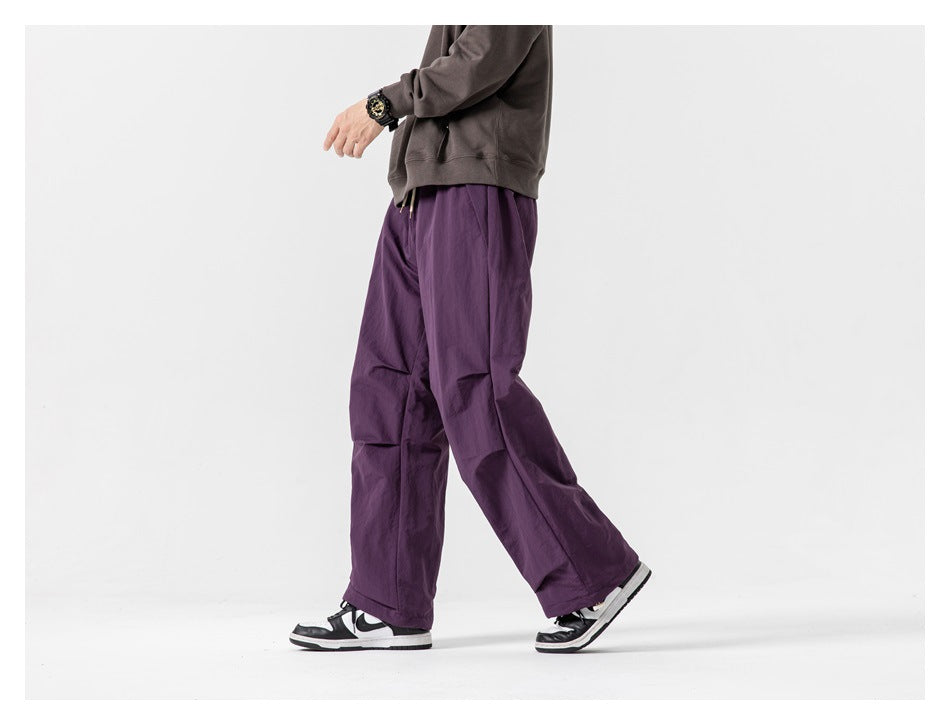 Cropped model walking in loose purple pants, shown from the side with black-and-white sneakers.
