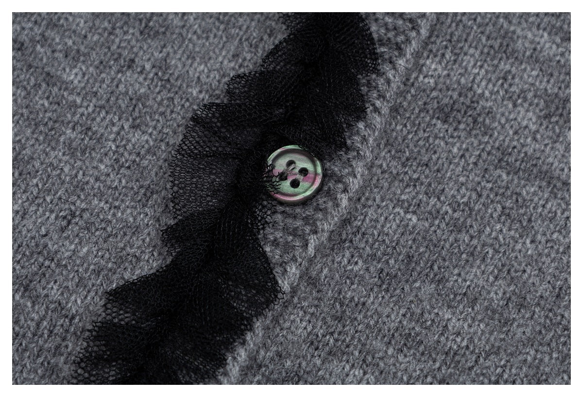Close-up of a gray knit cardigan button beside sheer black mesh ruffle trim.