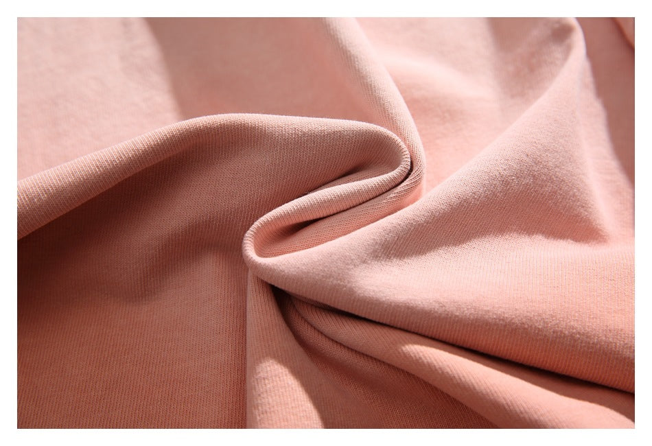 Close-up of peach-pink fabric draped into soft folds, showing its fine knit texture.