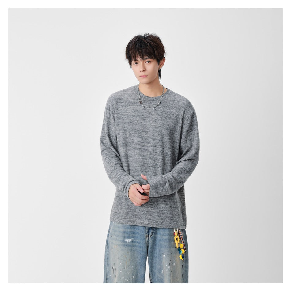 Model wearing gray heathered long-sleeve top with hands clasped, paired with paint-splattered jeans