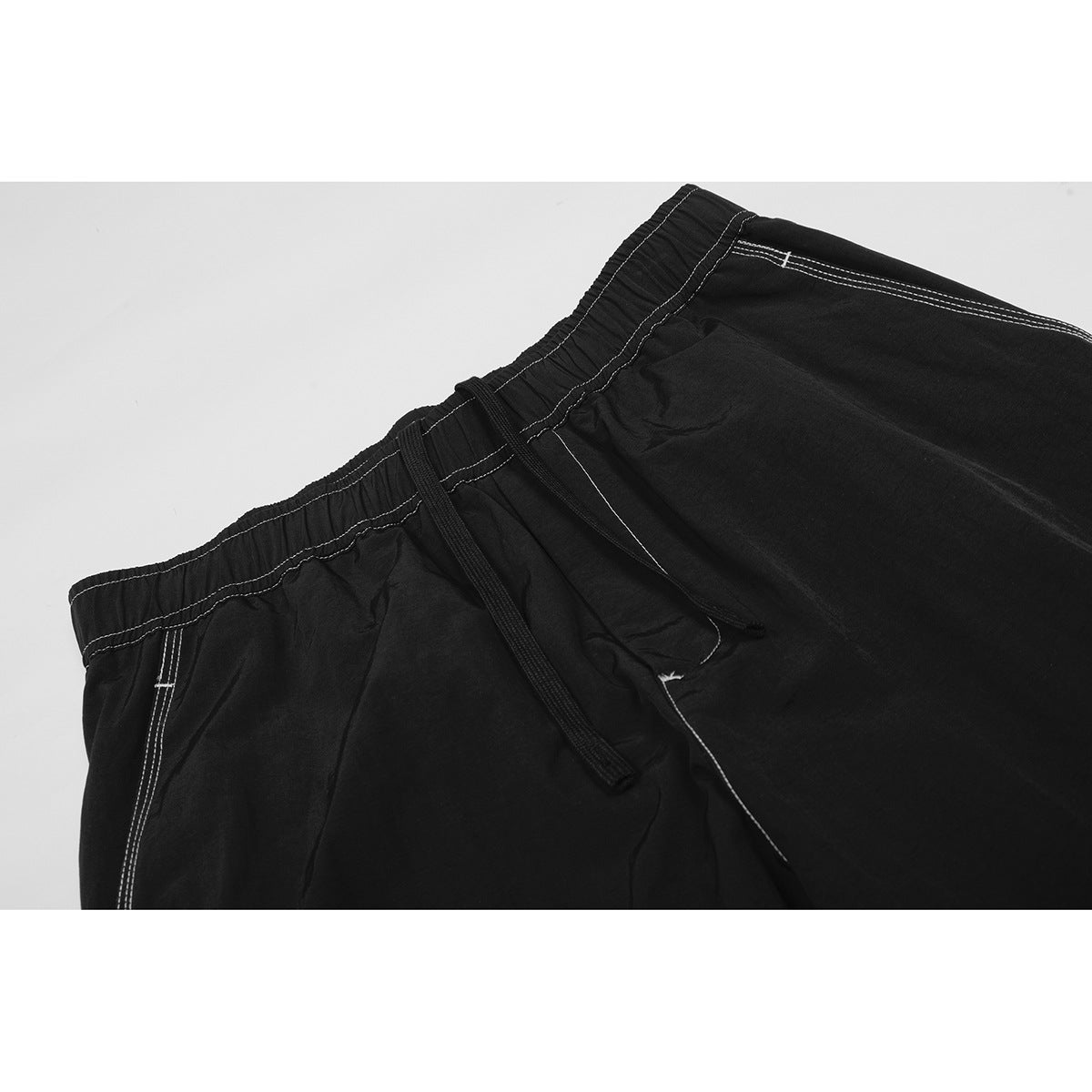Close-up of black pants with an elastic waistband, drawstring, and contrasting white stitching.