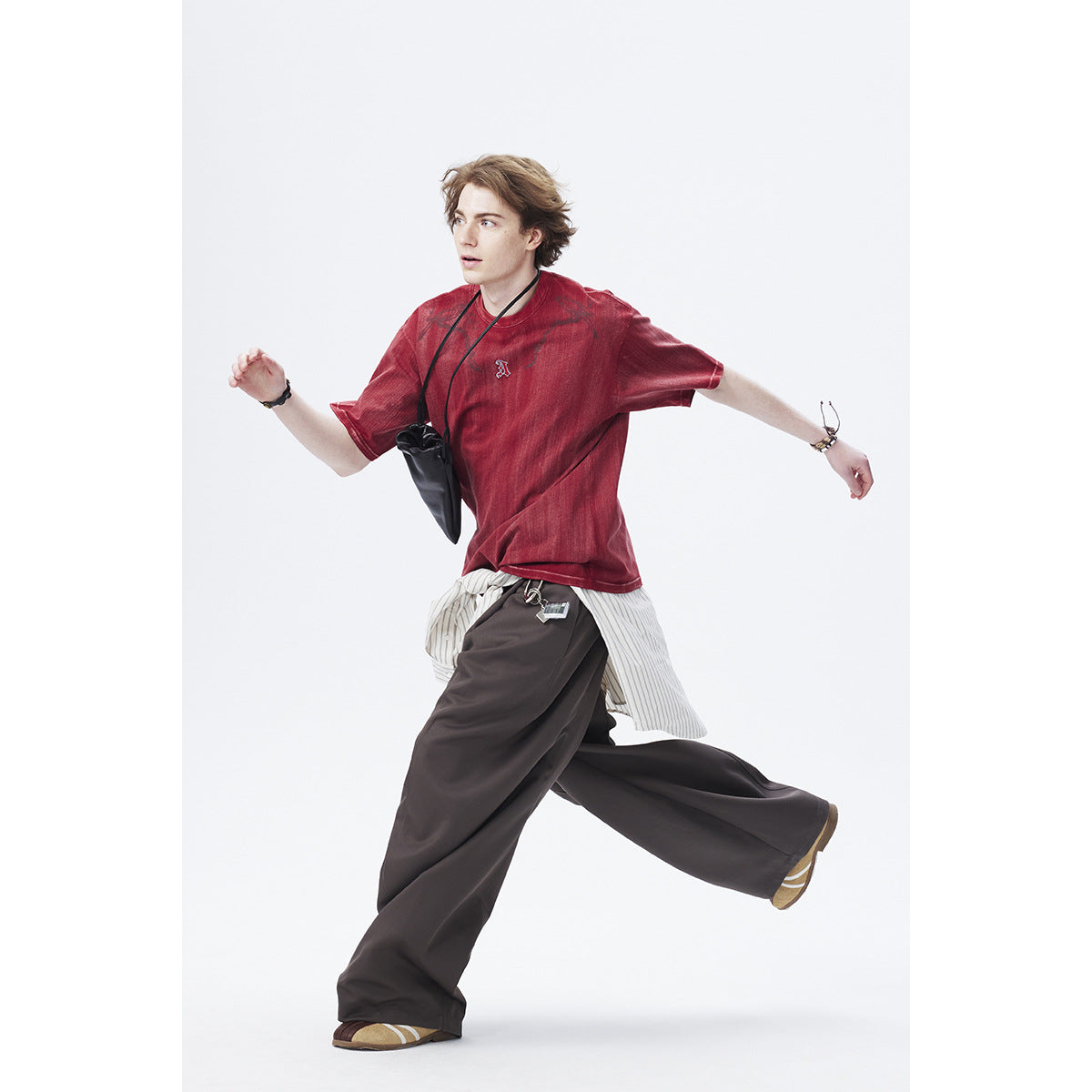 Model in a faded red graphic T-shirt and loose dark trousers, shown mid-stride against a white background.