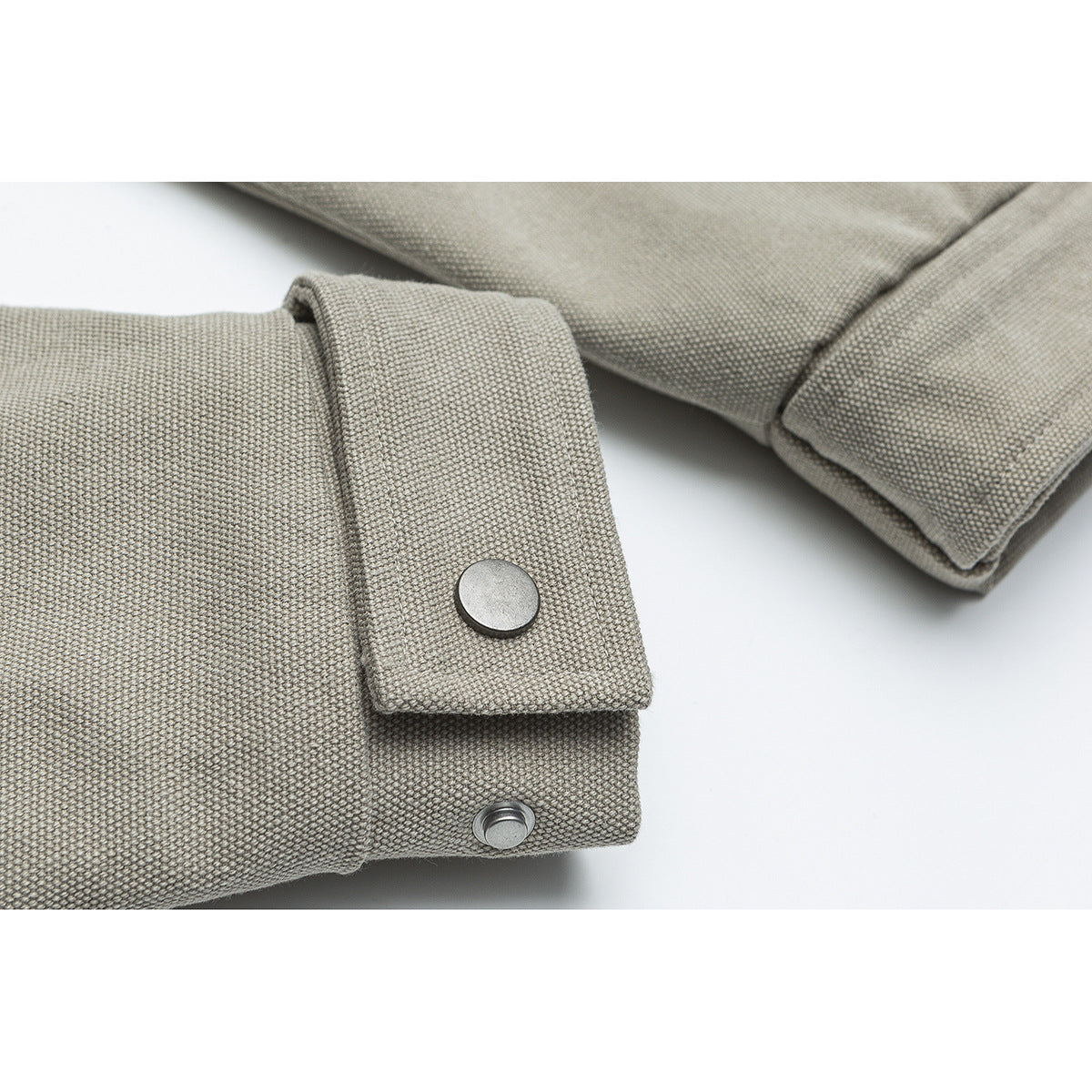 Close-up of a beige jacket sleeve cuff with a metal snap button.