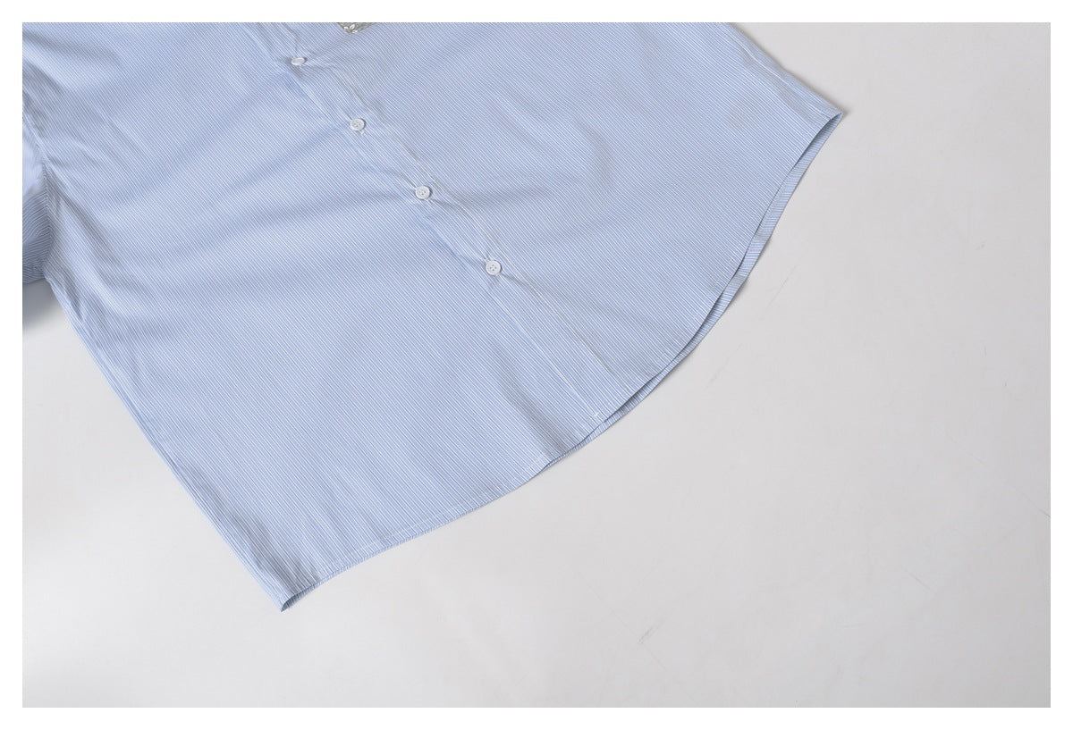 Cropped flat lay of a light blue pinstriped shirt showing its button placket and curved hem.