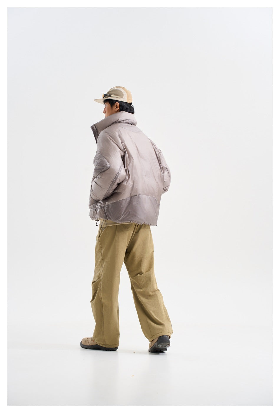 Rear three-quarter view of a model wearing a light gray puffer jacket with a high collar.