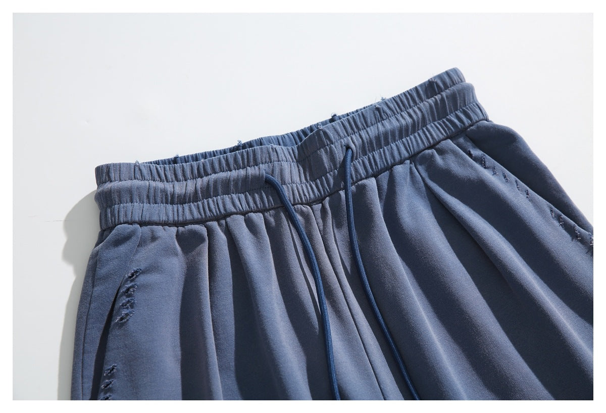 Close-up of slate-blue pants showing the gathered waistband, drawstrings, and distressed stitching.