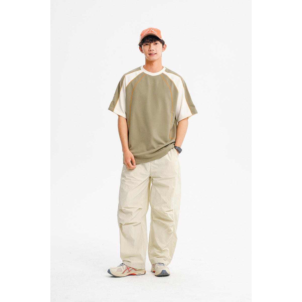 Front view of a model wearing an olive raglan T-shirt with cream sleeves and loose cream trousers.