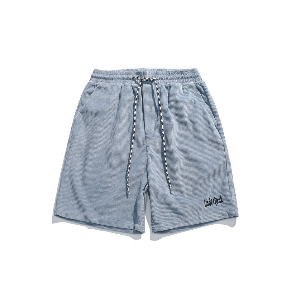 Hazy blue corduroy-style shorts with elastic waist, patterned drawstring and small dark embroidered text, flat lay
