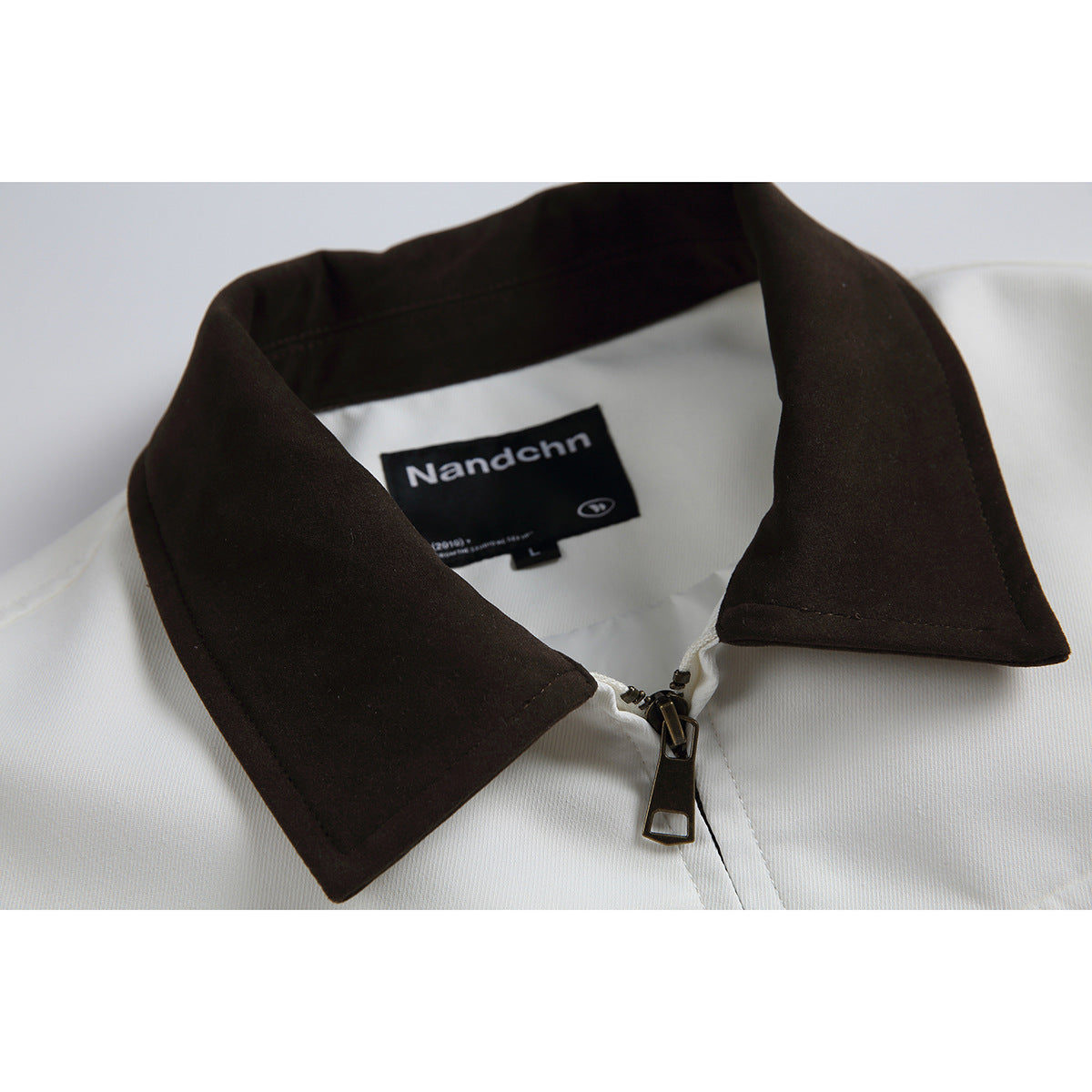 Close-up of a white garment with a dark brown collar, zipper, and visible black neck label.