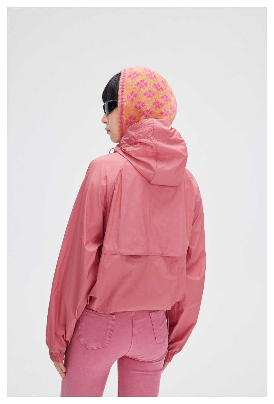 Back view of a rose-pink hooded jacket worn with pink trousers; the jacket has a back vent panel and elastic cuffs.