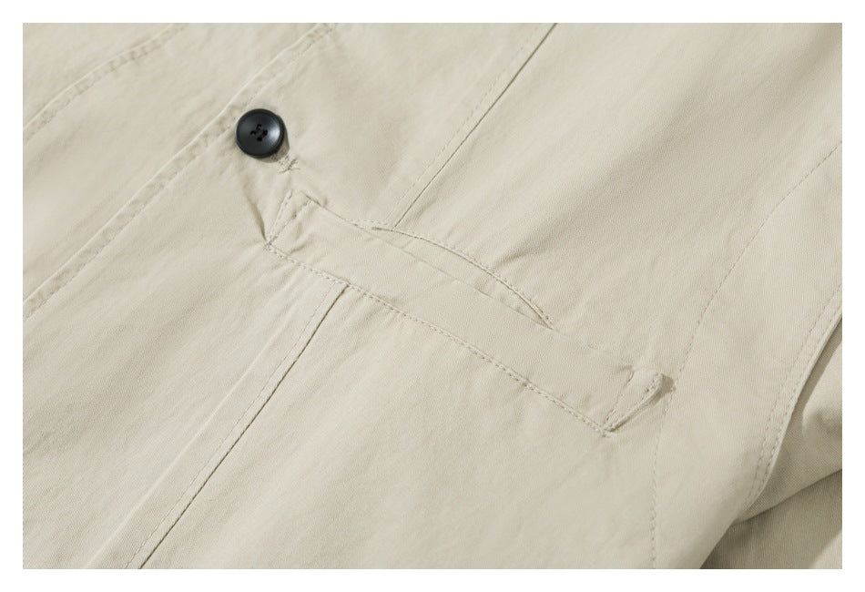 Close-up of a pale beige garment's slanted welt pocket and black button.