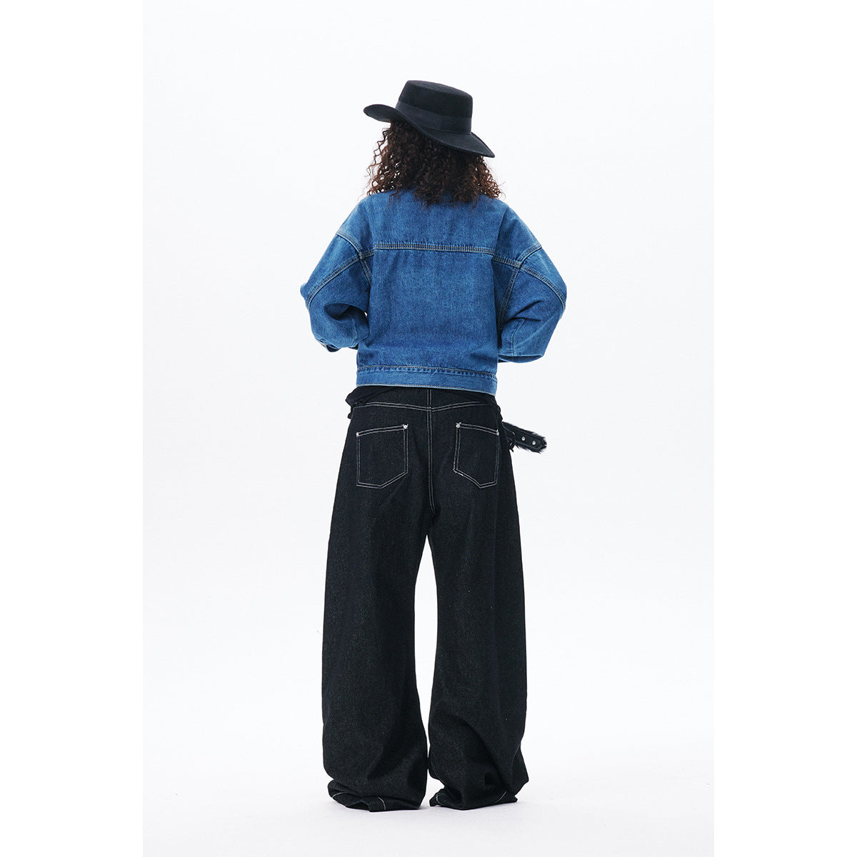 Back view of a model wearing a blue denim jacket and black wide-leg jeans with rear pockets and contrast stitching.