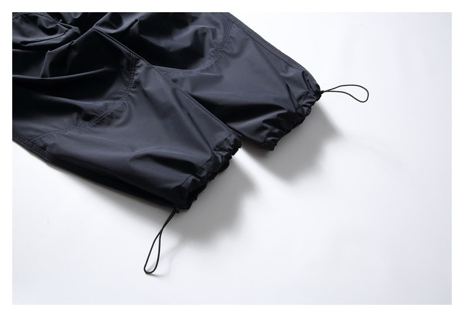 Close-up of two dark trouser cuffs with elasticated hems and looped drawcords.