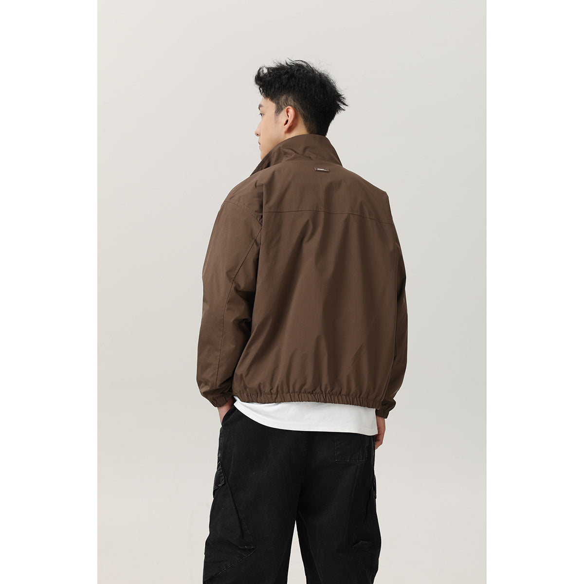 Back view of a model wearing a brown jacket with a raised collar and gathered hem.