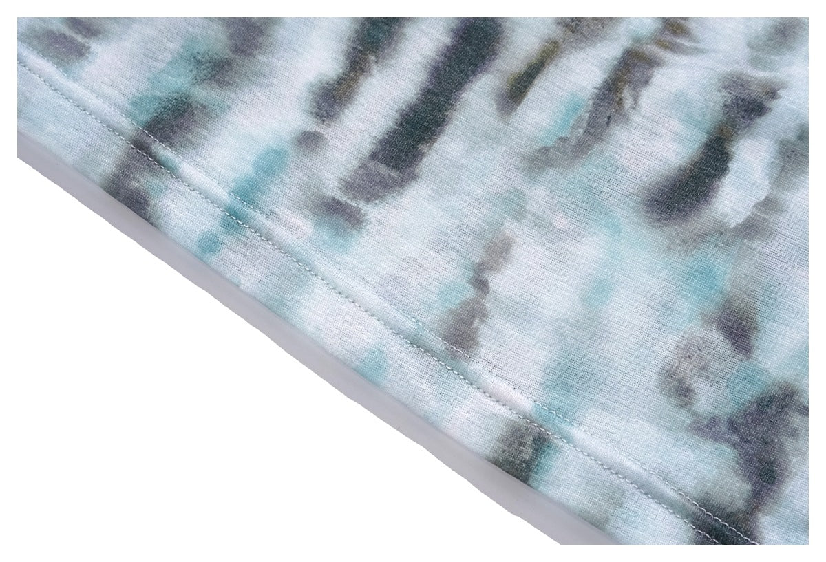Close-up of a diagonal stitched hem on pale aqua, gray, and dark tie-dye fabric.