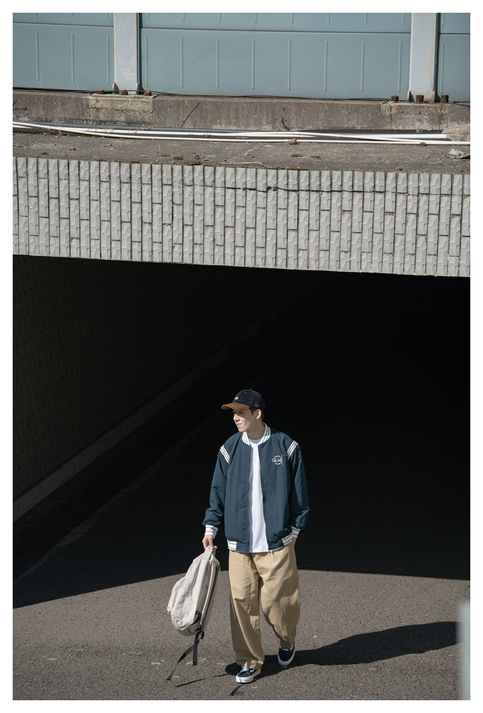 A model wears a dark teal jacket with white striped trim and a chest design, paired with beige trousers.