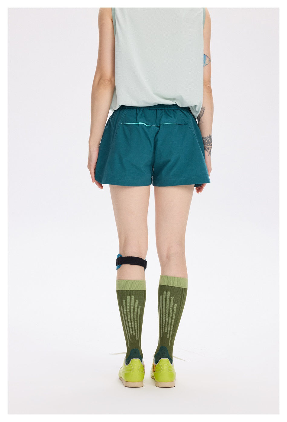 Rear view of a model wearing teal running shorts with an elastic waistband and a small back pocket with turquoise trim.