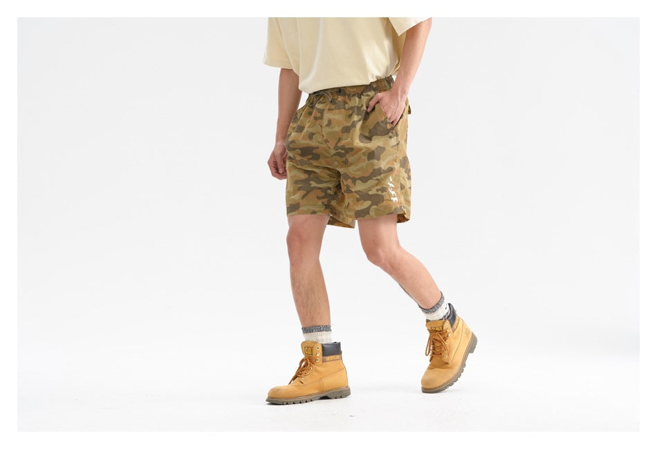 Model wearing olive and brown camouflage drawstring shorts, shown from the front at an angle.