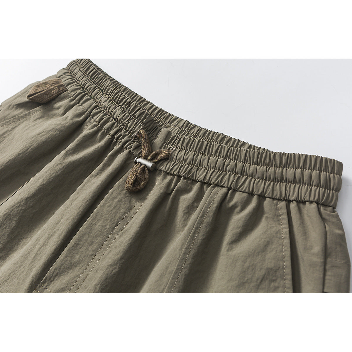 Close-up of olive-gray shorts with a gathered elastic waistband and brown drawcord.