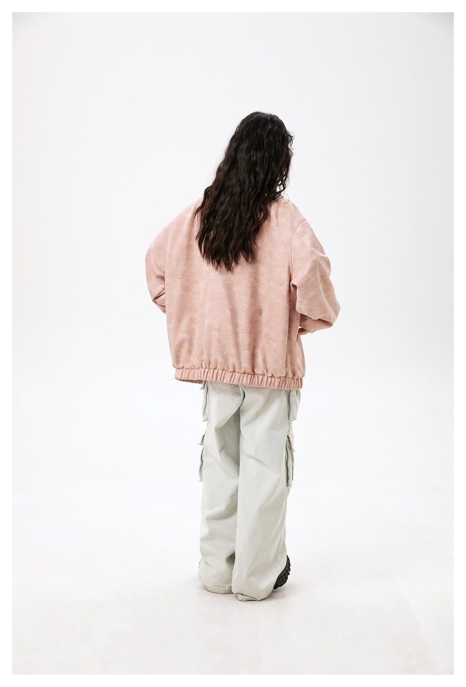 Back view of a model wearing a dusty pink jacket with an elastic hem and pale cargo pants.