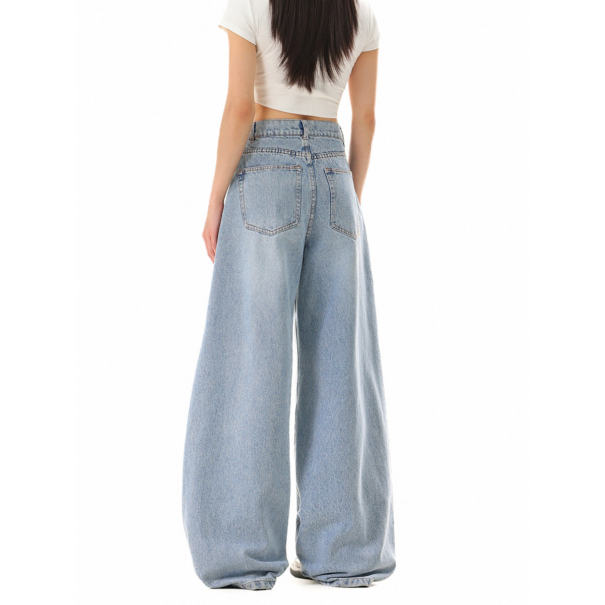 Back view of a model wearing light-wash, very wide-leg jeans with two back pockets and a white cropped T-shirt.