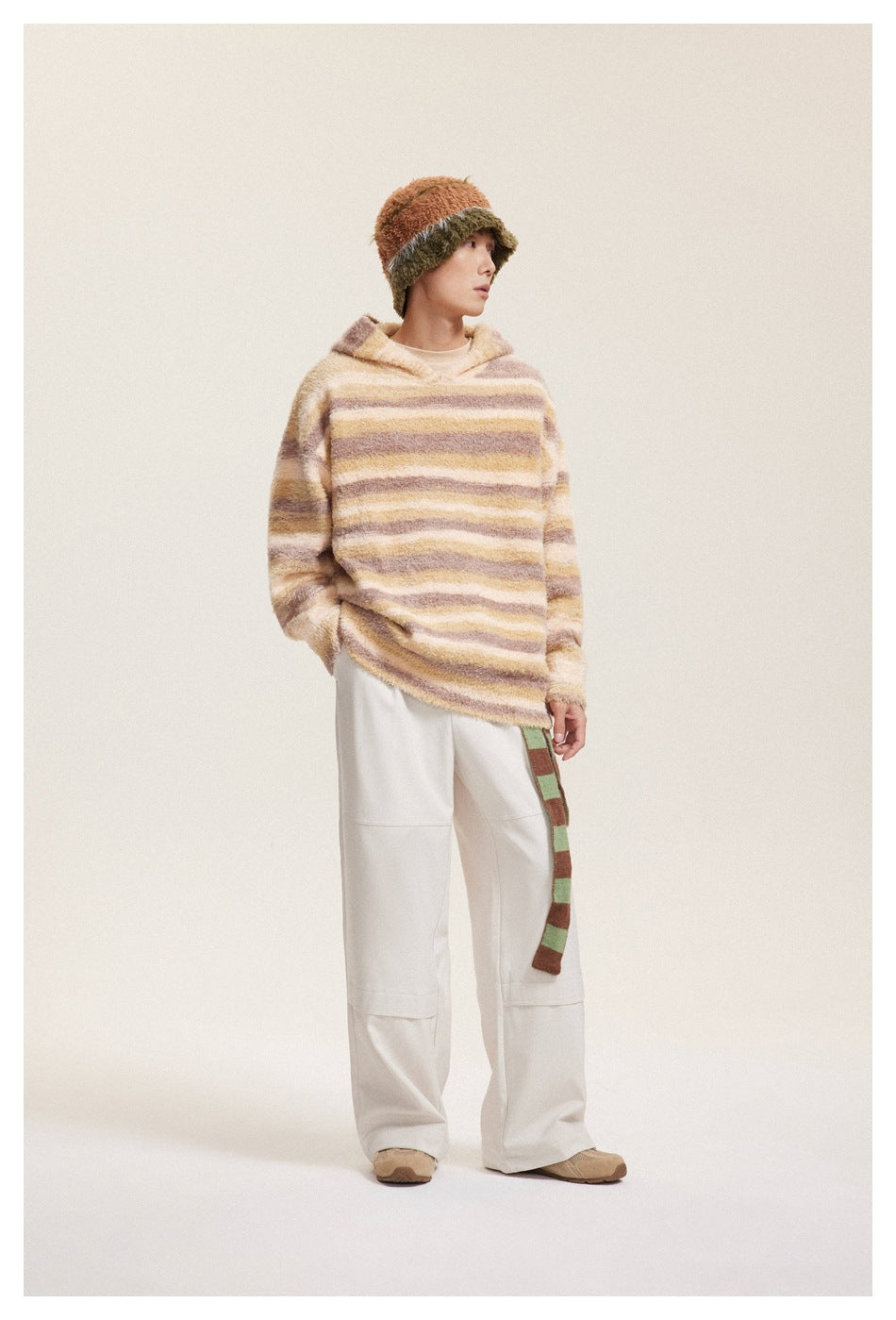 Full-length view of a model wearing a cream, tan, and mauve striped fuzzy hooded pullover.