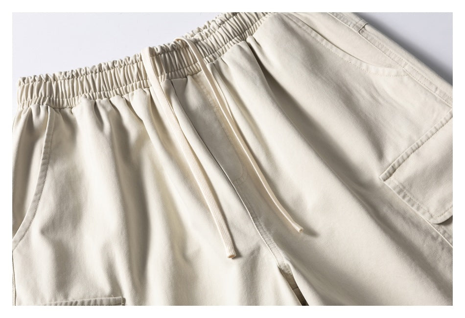 Close-up of cream shorts’ front with an elastic waistband, long drawstrings, and part of a cargo pocket.