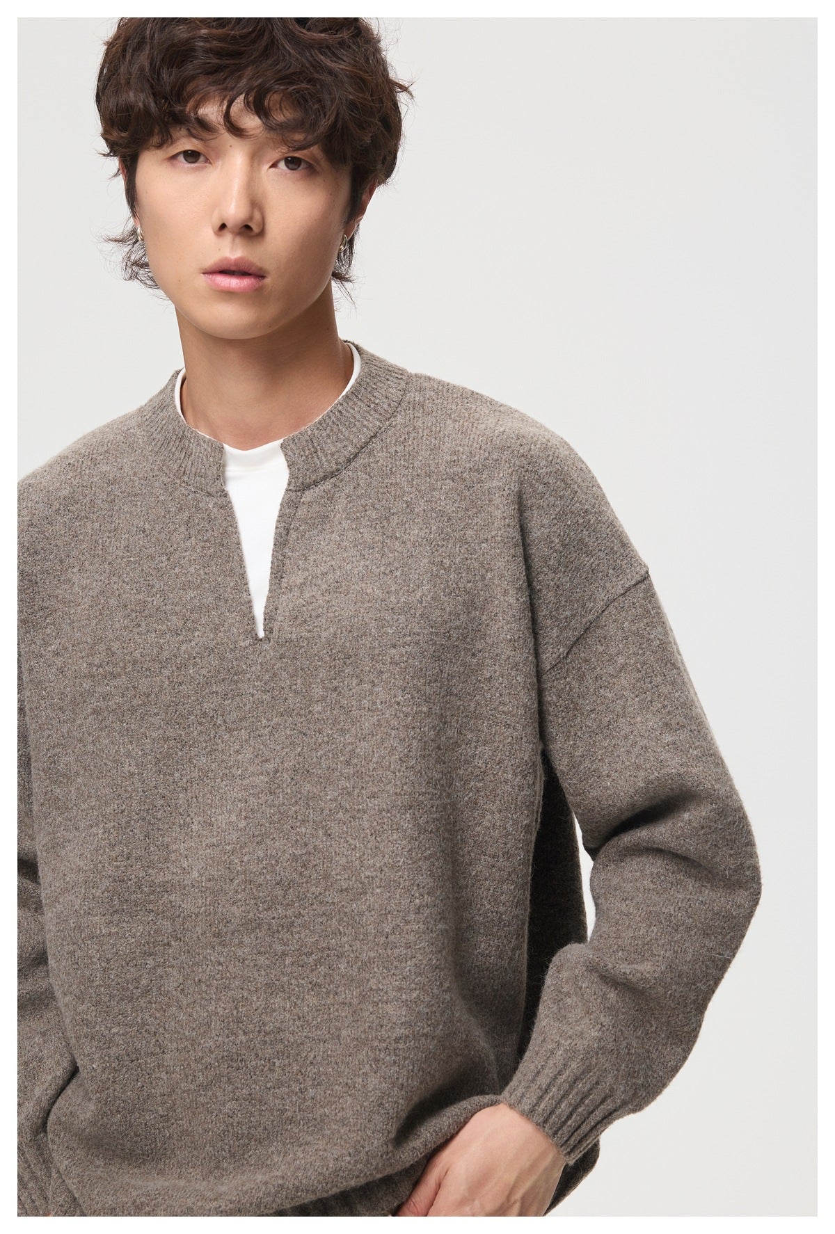 Close-up of a model wearing a taupe sweater with a split neckline and ribbed collar and cuffs.