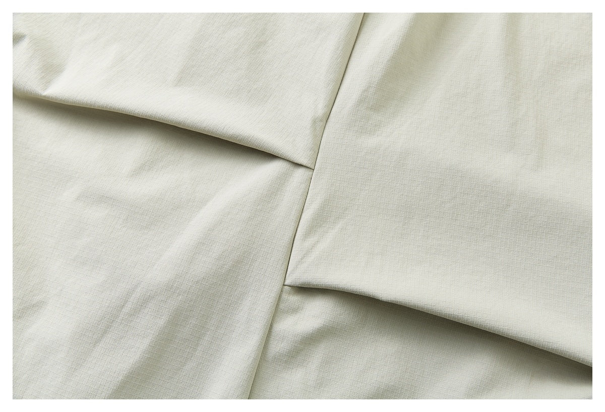 Close-up of pale khaki garment panels overlapping at a seam, with the fine fabric texture visible.