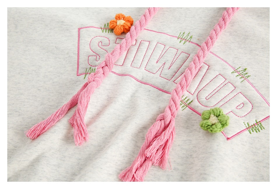 Close-up of pink braided drawstrings over outlined pink lettering and small colorful flower embroidery on gray heather