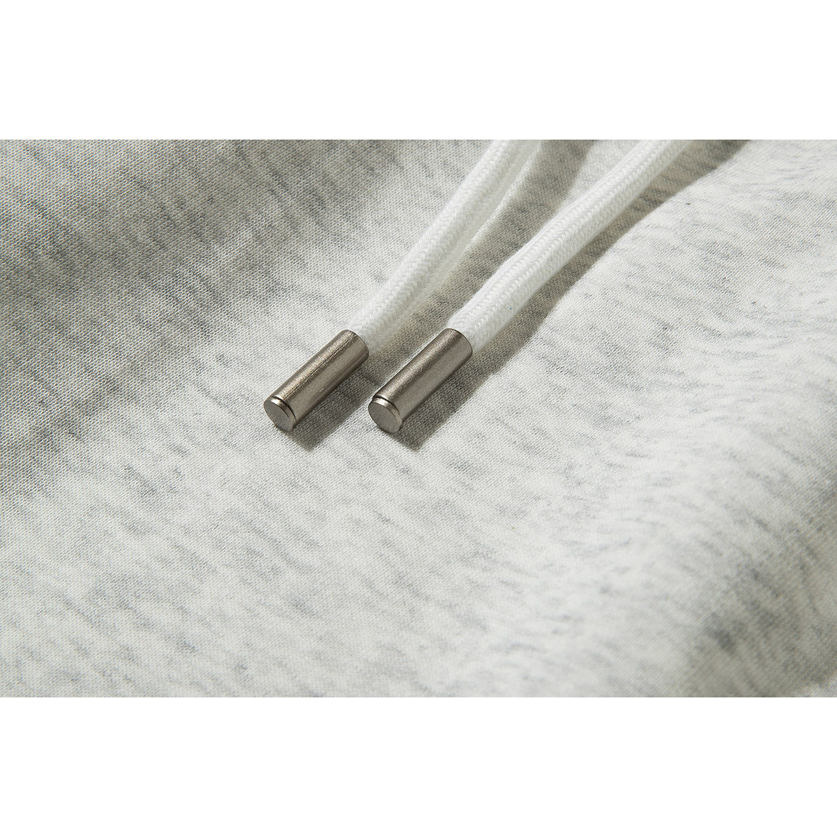 Close-up of two white drawstrings with metal tips on light gray mottled fabric.