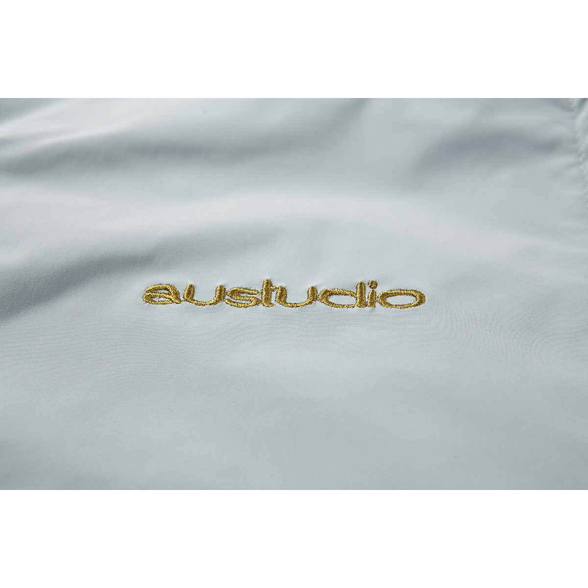Close-up of gold embroidered lettering on pale blue-gray garment fabric.