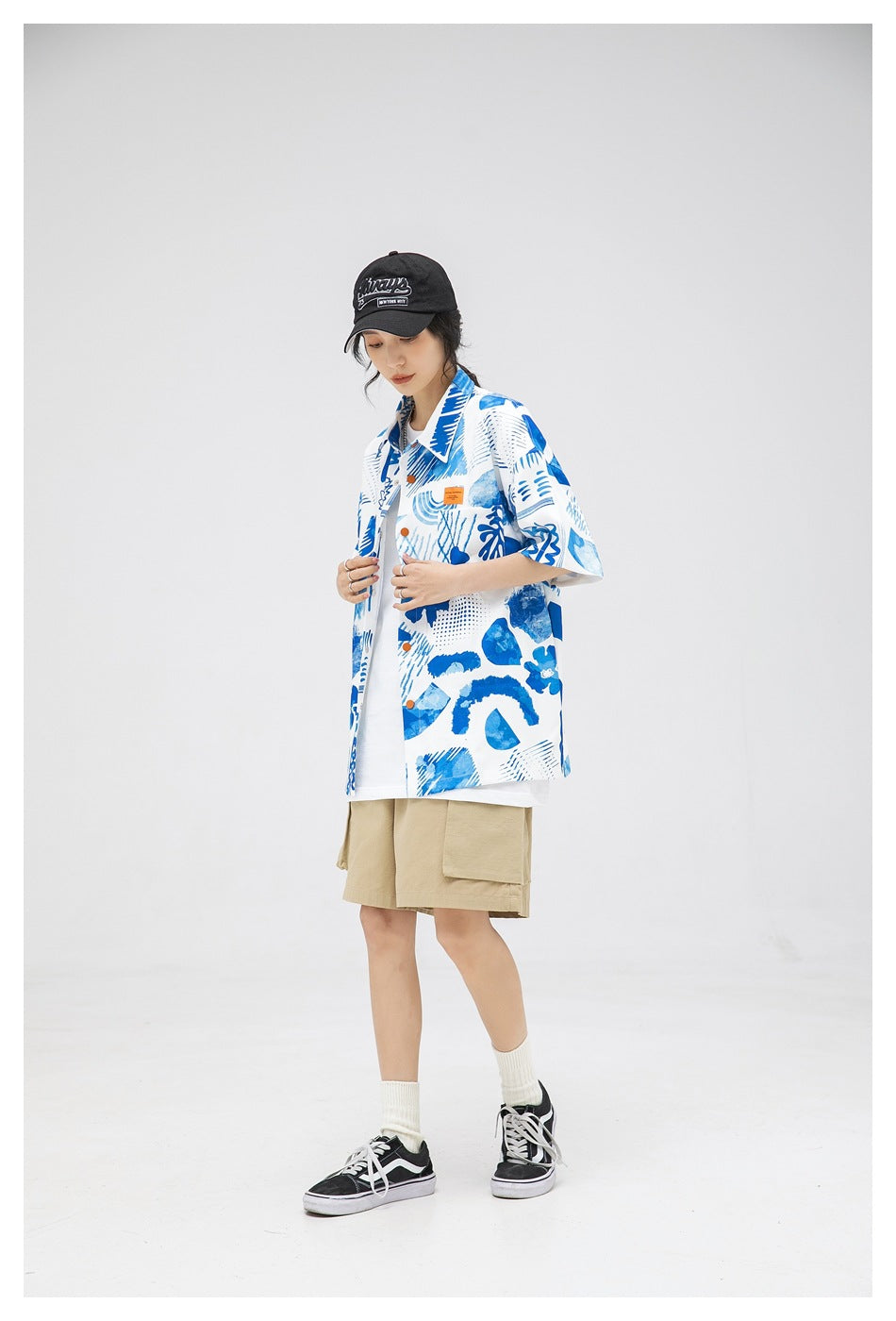 Model wearing an open blue-and-white abstract print shirt over a white tee with beige shorts.