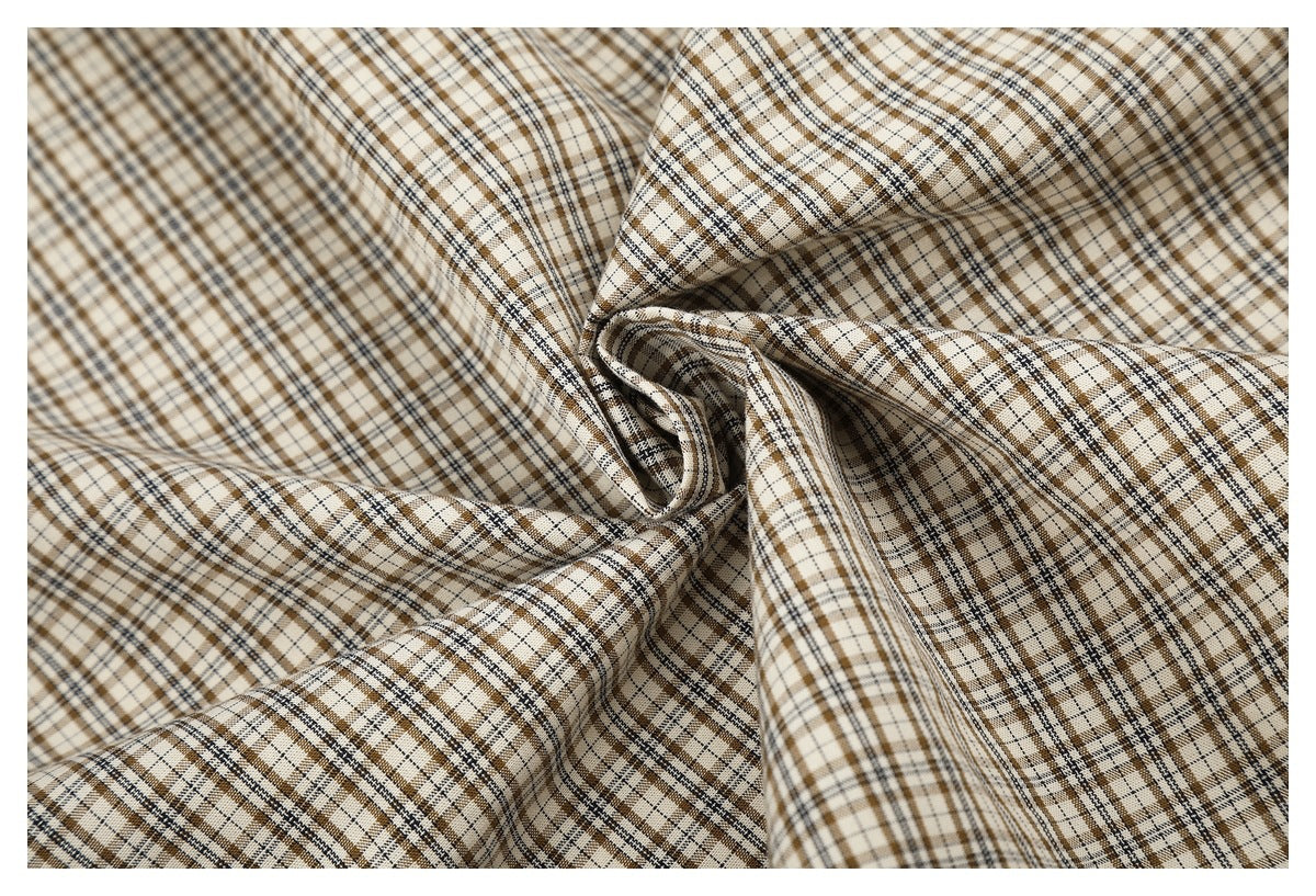 Close-up of cream fabric with a brown and black plaid pattern, arranged in soft folds.