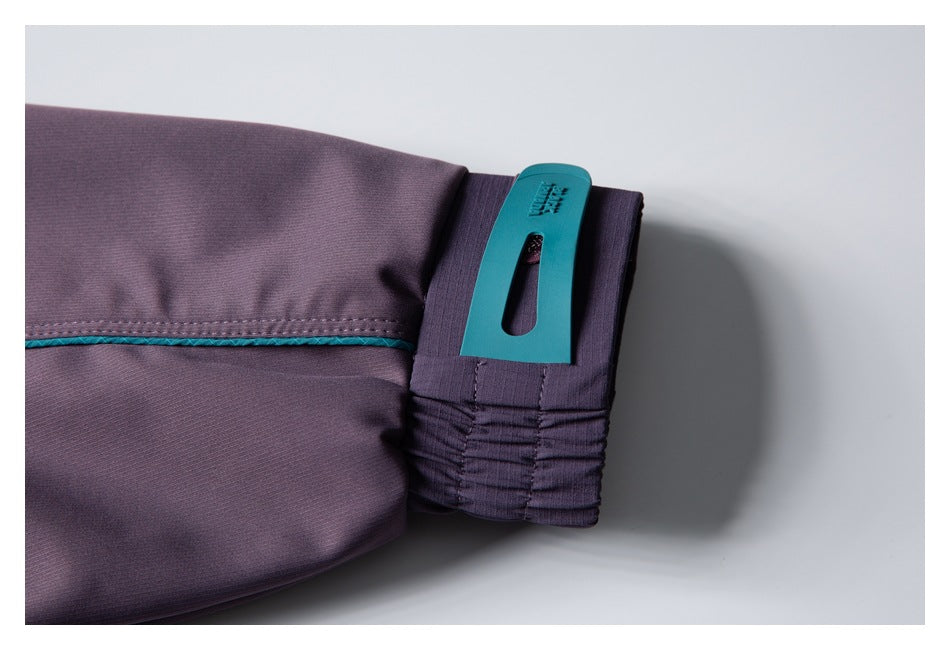 Close-up of a plum jacket cuff with gathered stitching, teal piping, and a teal fastening tab.