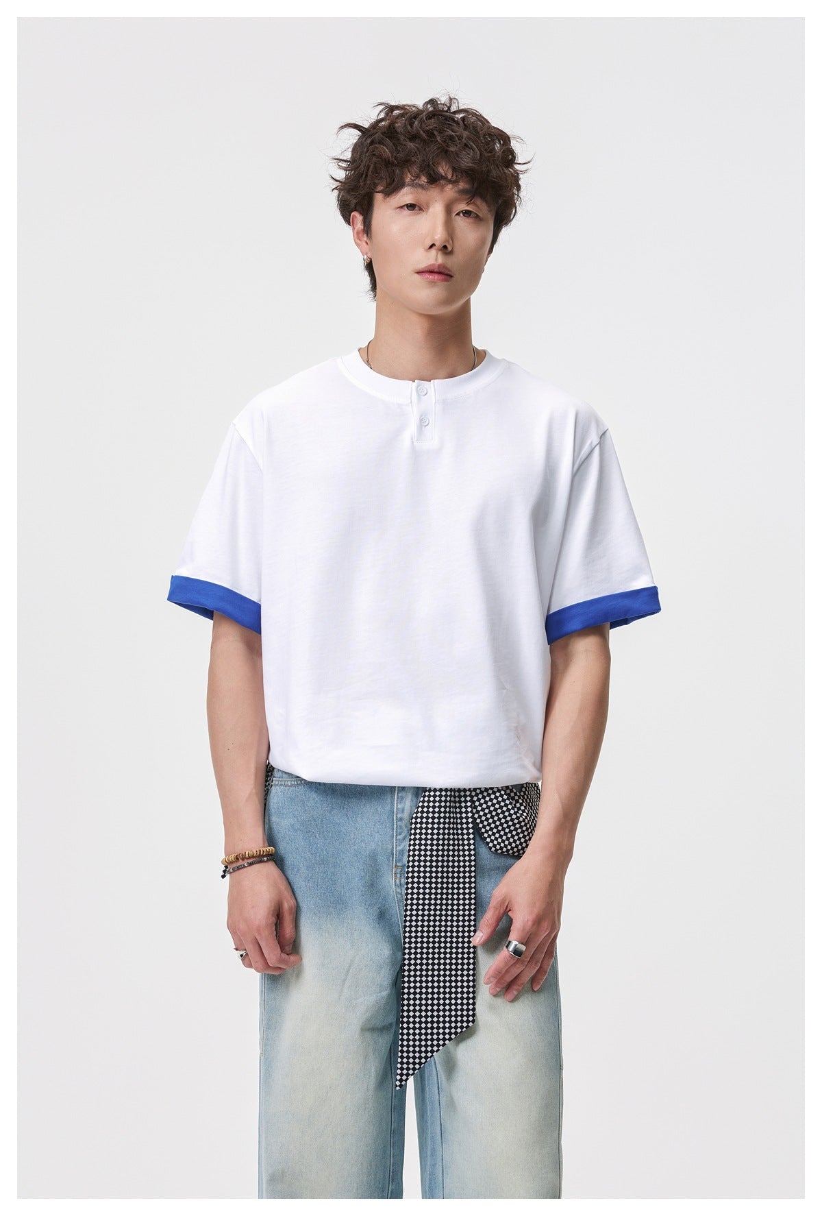 Closer front view of a model wearing a white henley T-shirt with blue turned-up sleeve cuffs and light-wash jeans.