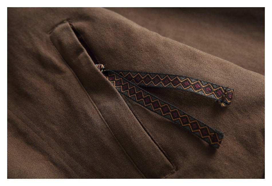 Close-up of brown garment fabric with a pocket and patterned trim.