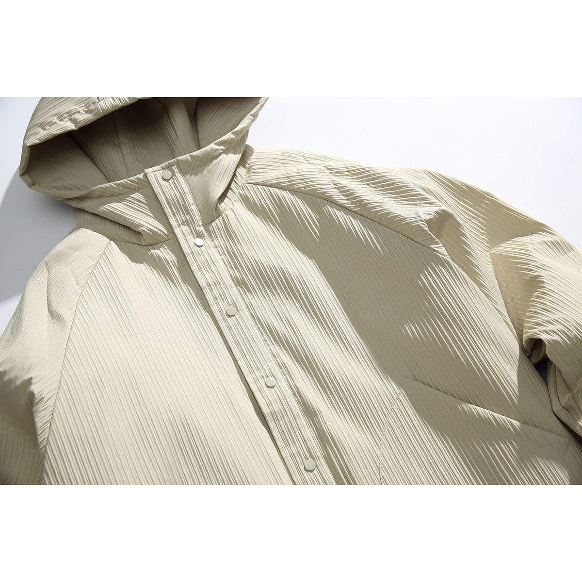 Close-up of an ivory hooded jacket showing its pleated texture, snap-button placket, and hood.