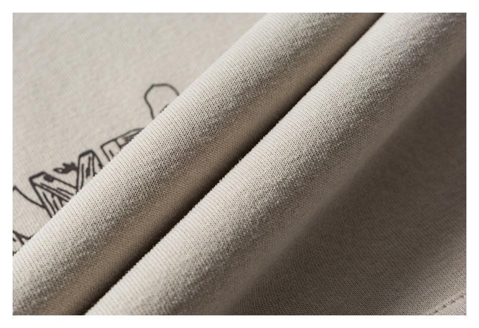 Close-up of folded cream hoodie fabric with part of a black camping illustration visible beneath the folds.